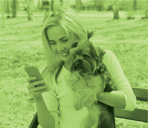Millenial woman holding her dog and looking at her phone.